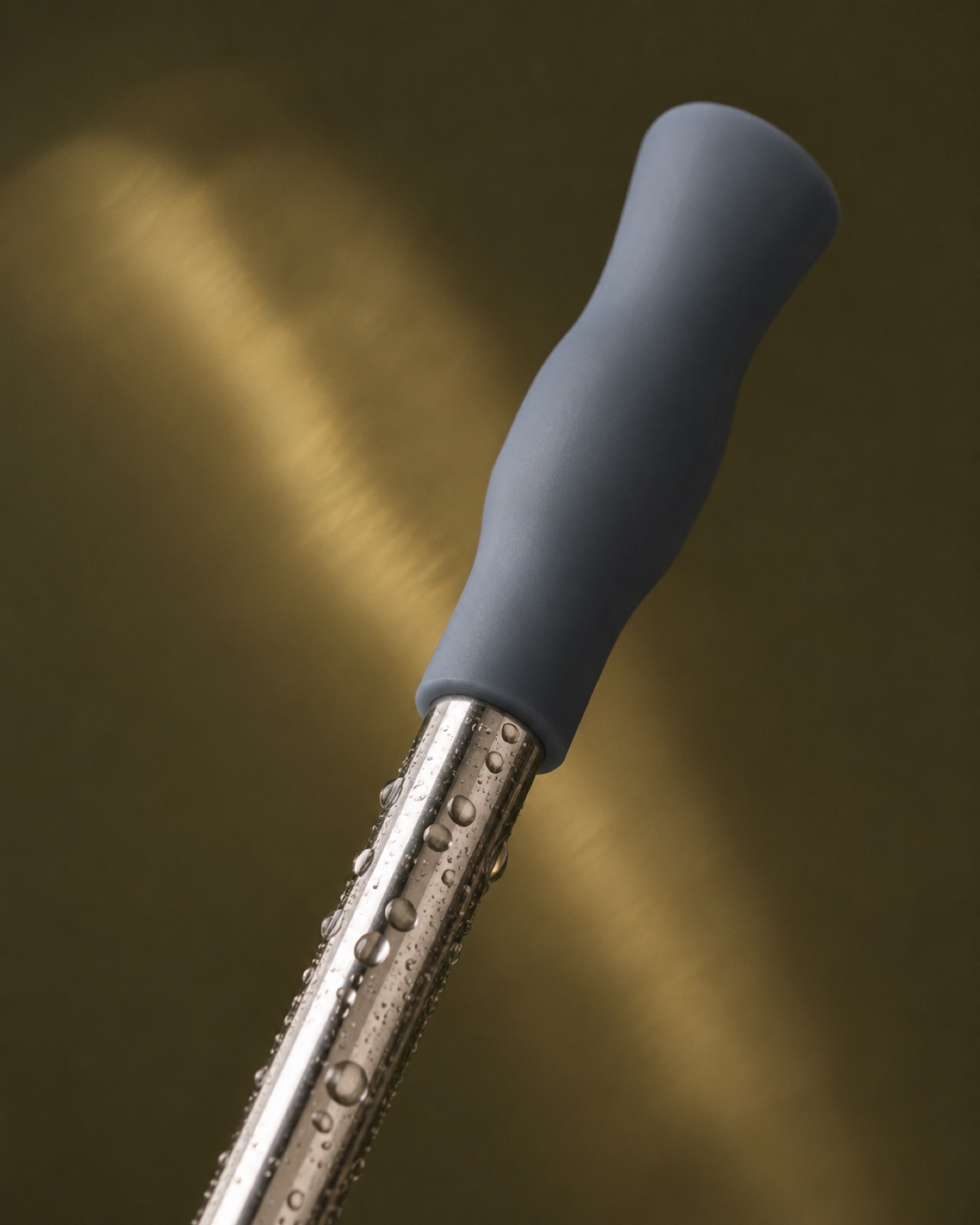 Macro close-up of a polished steel straw wearing a slate blue-grey silicone tip, beaded with water droplets